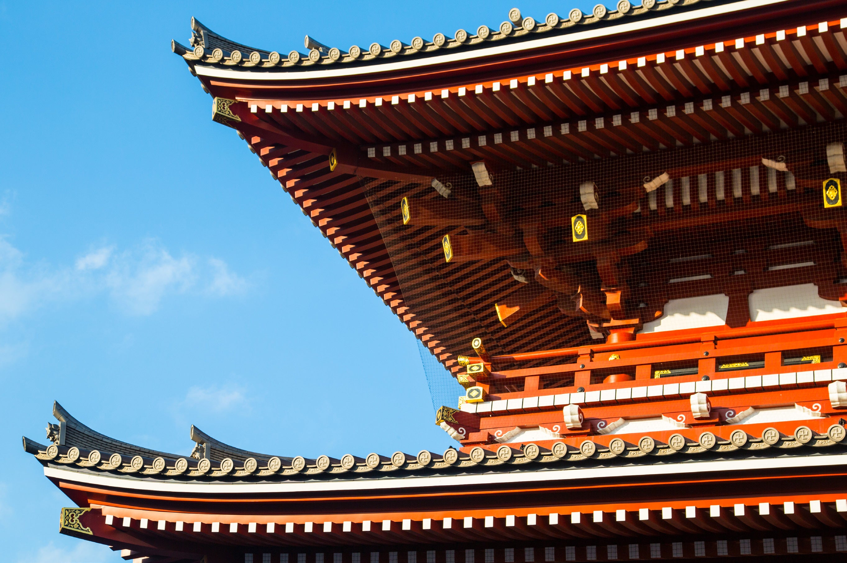 Close-up of ornate vermilion and black tiered roof eaves with gold decorative fittings on a traditional Japanese temple against a clear blue sky