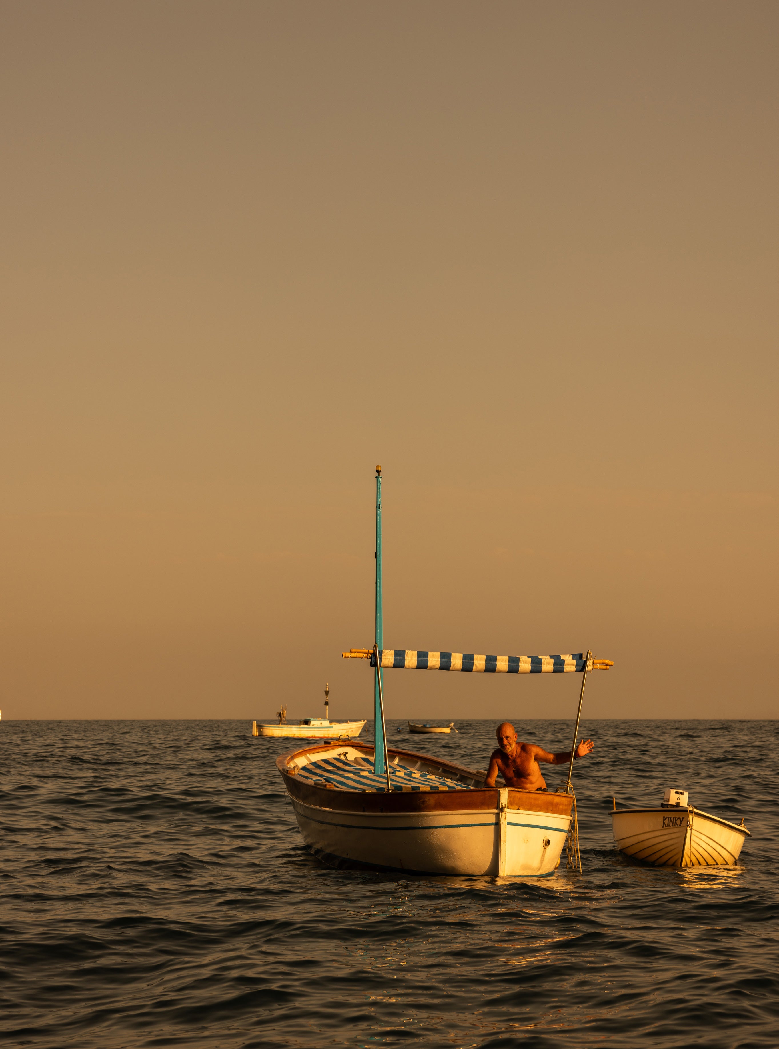 Fisherman in a traditional wooden boat with blue and white striped canopy at golden hour on calm Mediterranean waters