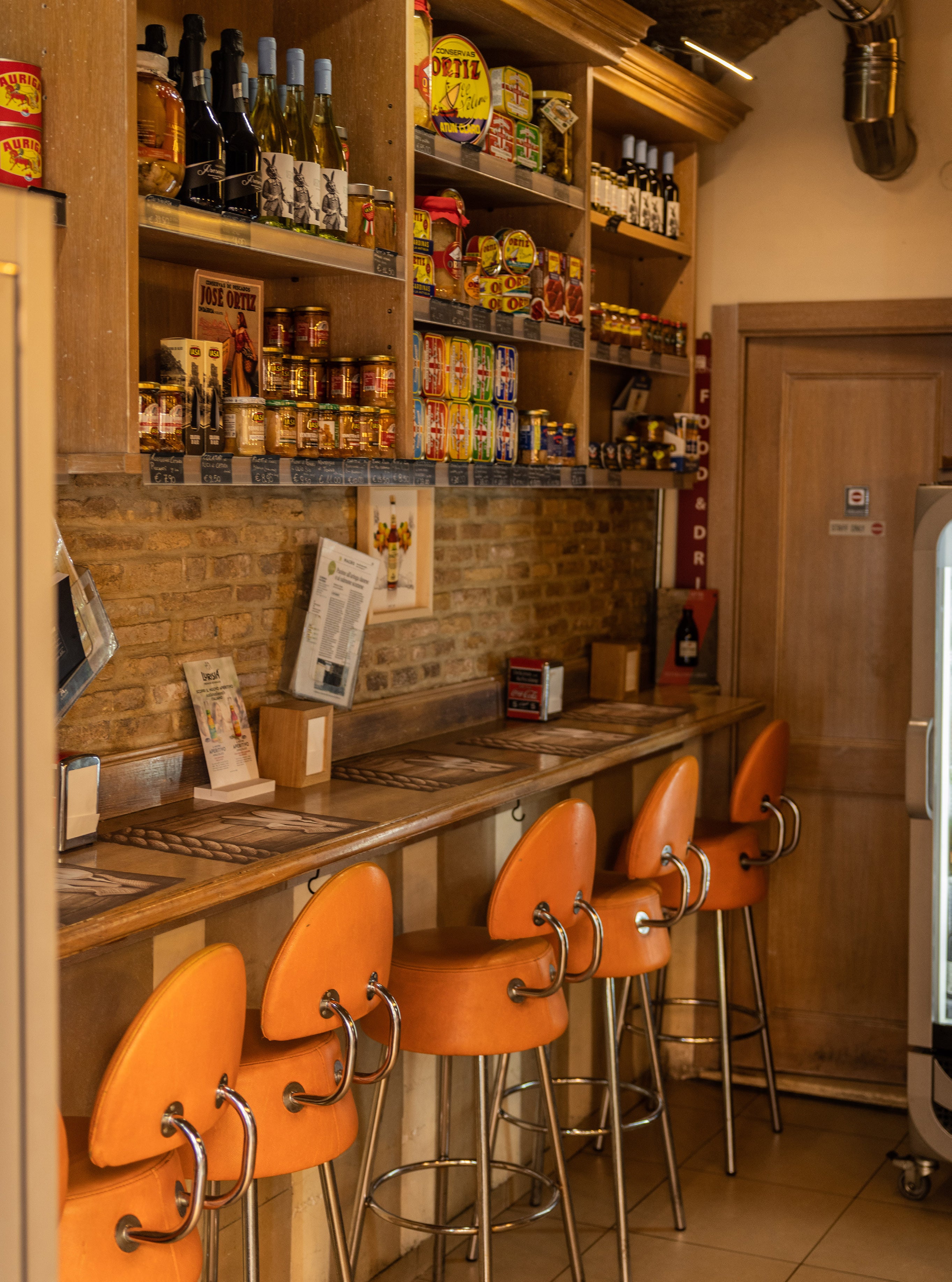 Interior of a traditional Italian bar with four bright orange retro stools at a wooden counter and shelves of bottles behind
