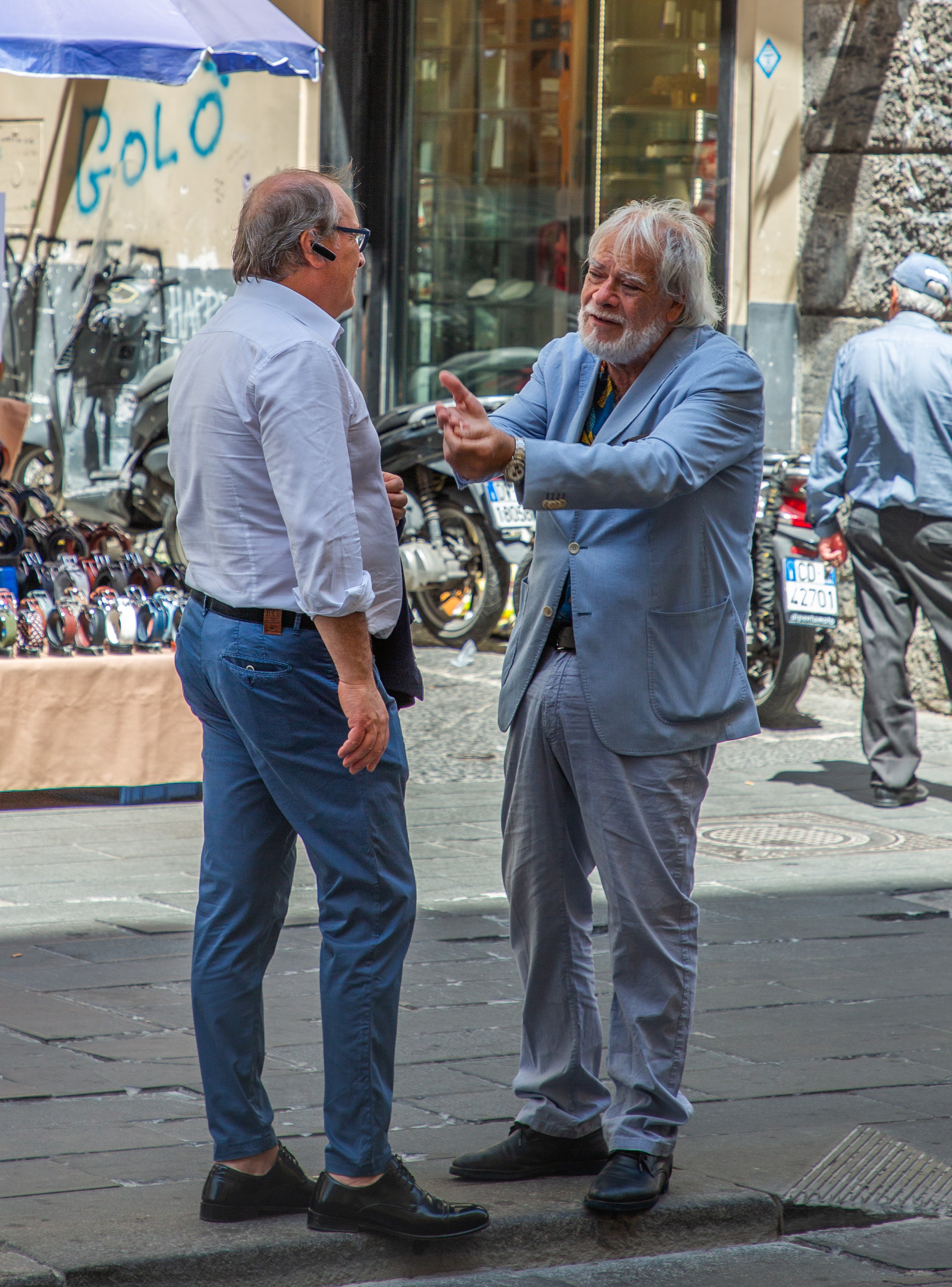 Two well-dressed men in animated conversation gesturing with their hands on a street in Naples
