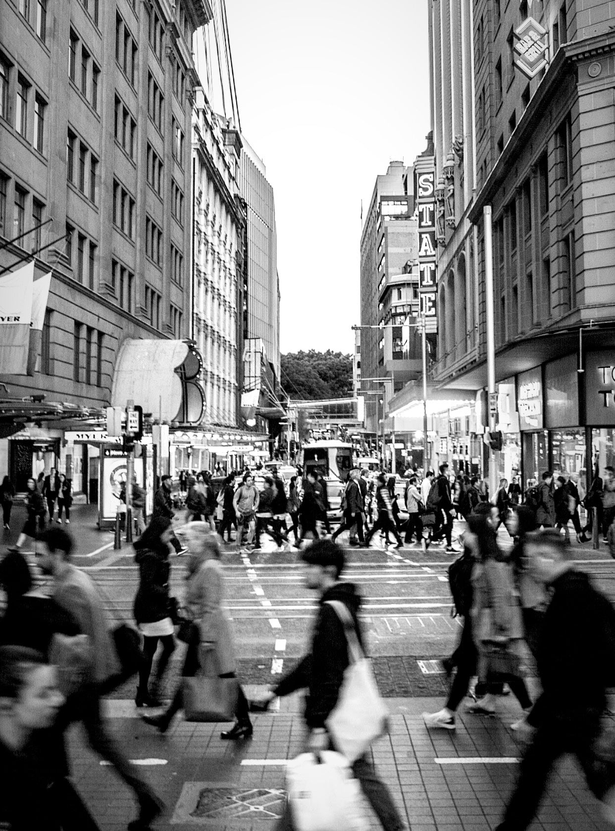 Black and white long exposure of pedestrians crossing a busy Sydney CBD intersection with the State Theatre sign in the background