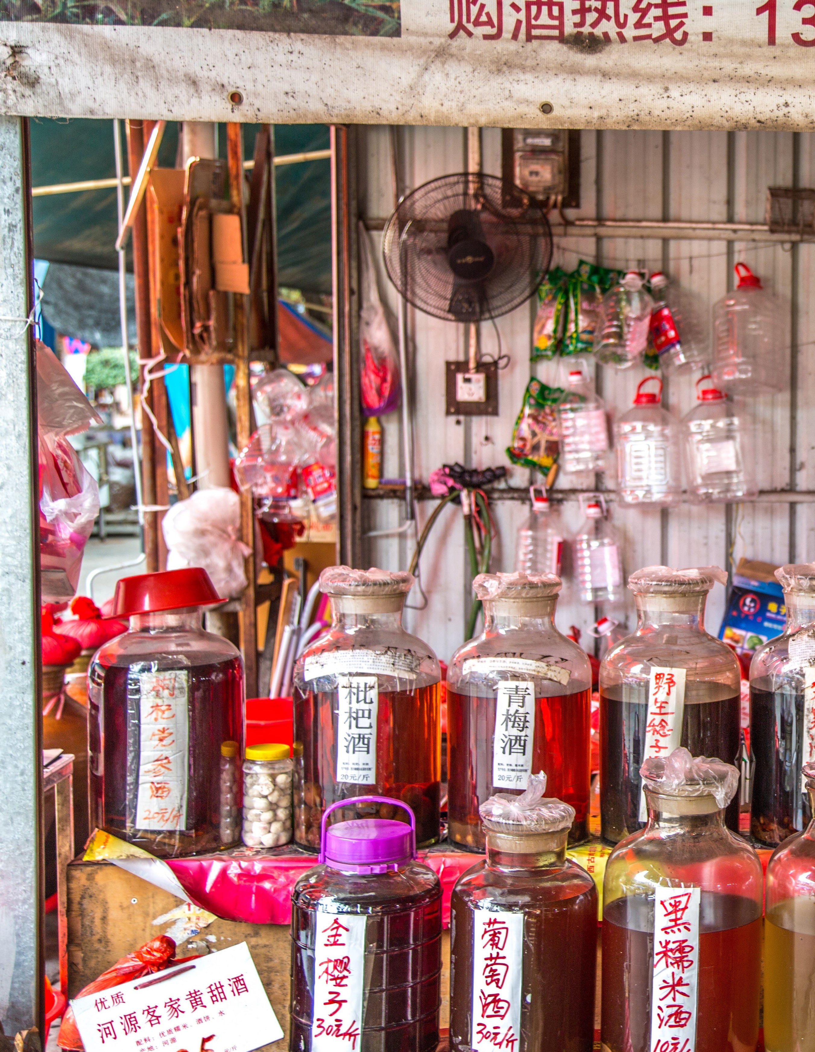 Collection of large glass bottles and jars containing amber and ruby infused spirits with handwritten Chinese labels at a market stall