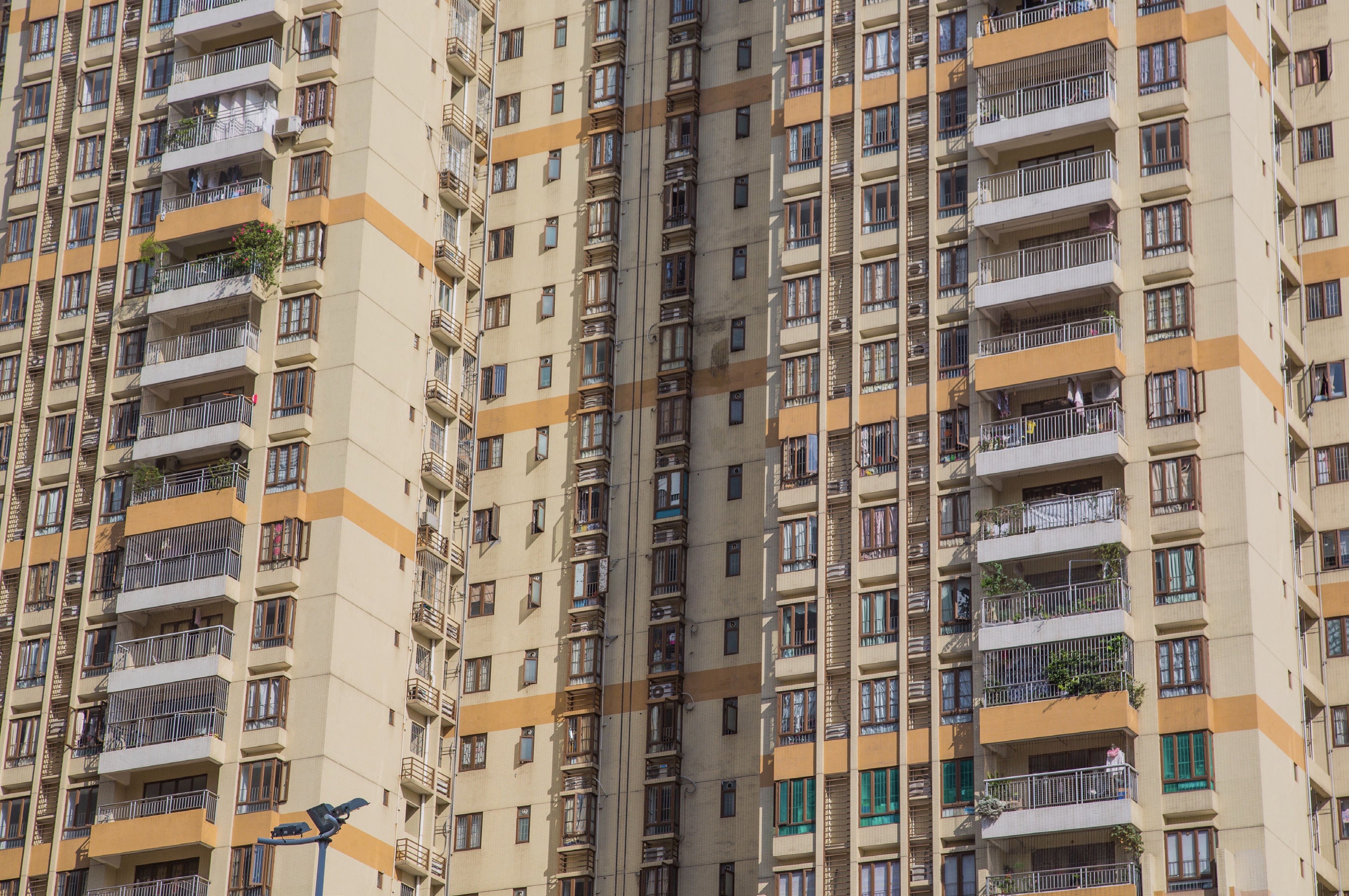 Close-up of a tall residential apartment building showing dozens of identical balconies in a geometric grid with cream walls and orange bands