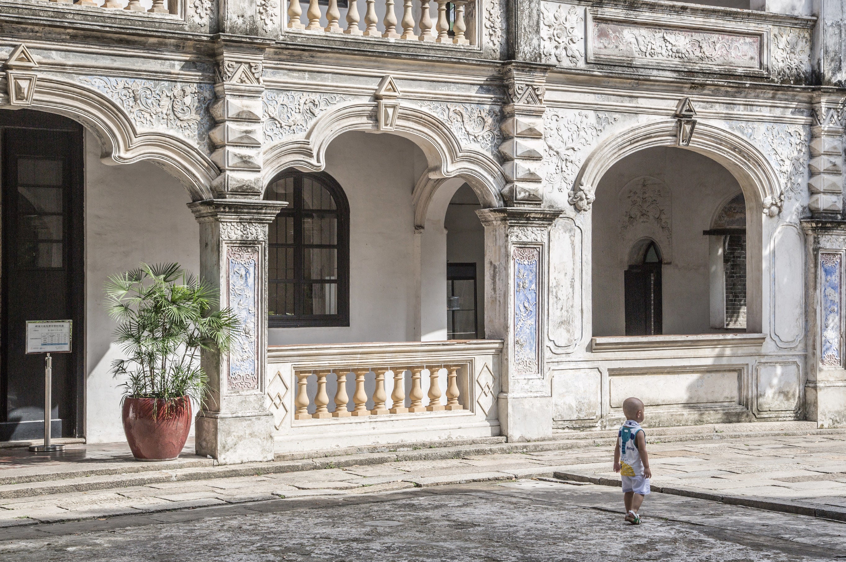 Small child walking in front of an ornate colonial building with carved stone arches decorative blue and white tiles and a potted palm