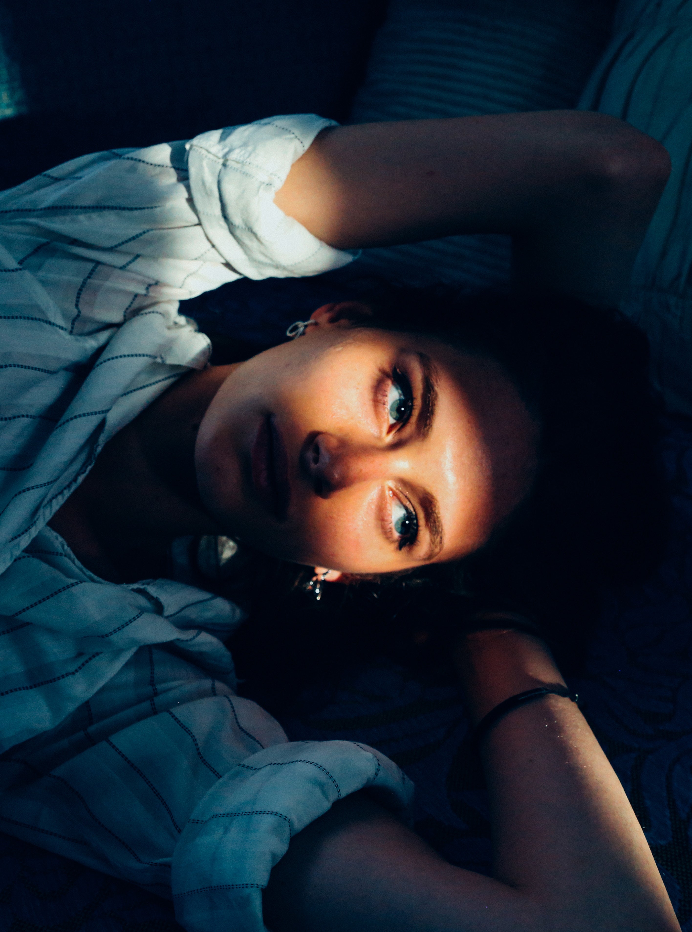 Dramatic portrait of a young woman lying down with a narrow beam of warm light illuminating her face against deep shadow