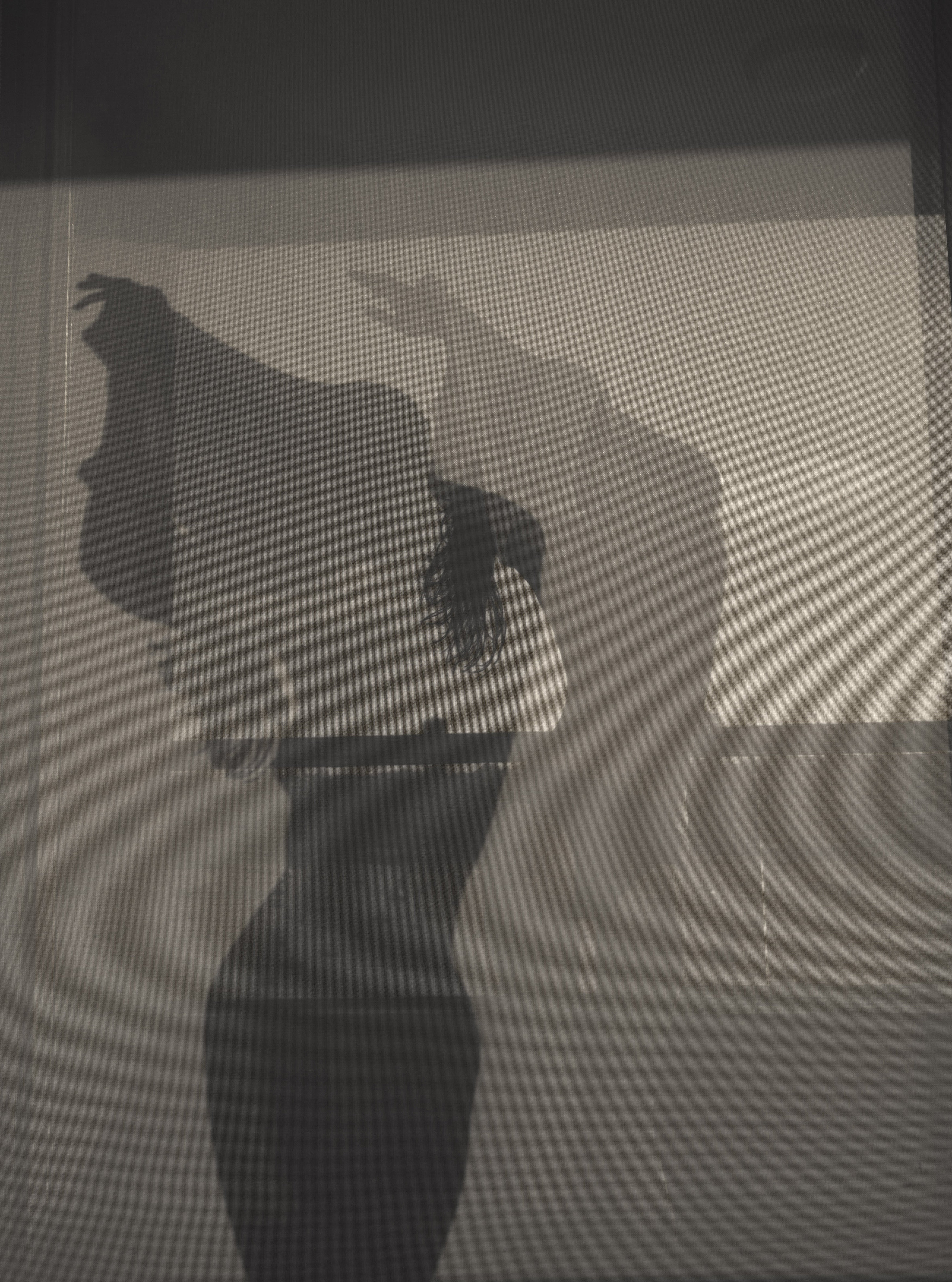Shadowy silhouette of a woman with arms raised seen through frosted or translucent glass in a dimly lit interior
