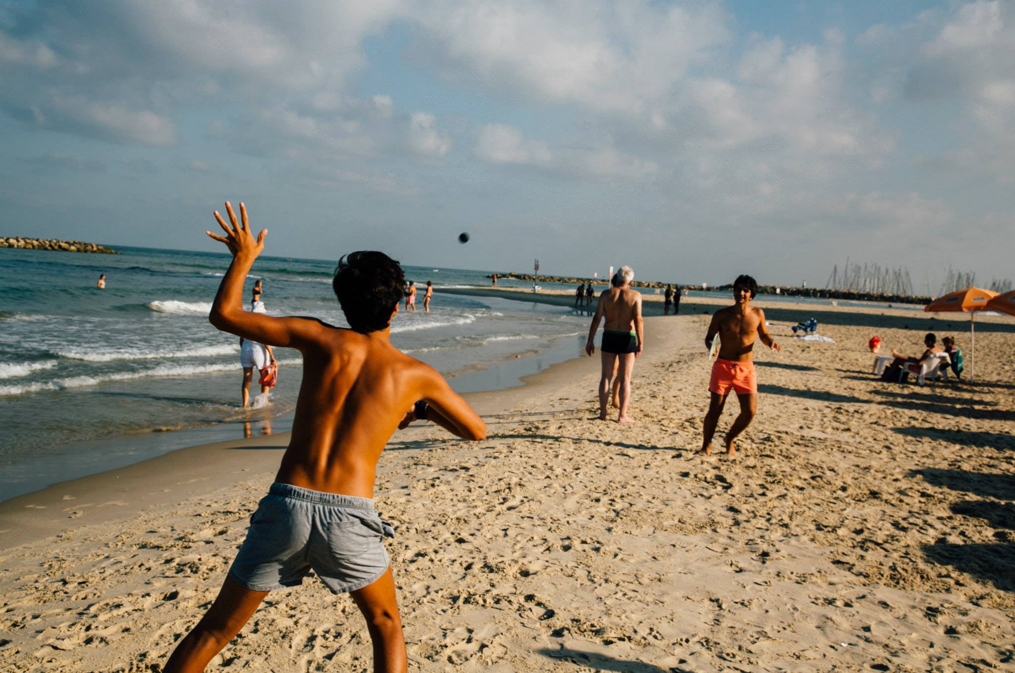 Young boys playing matkot paddle ball on the sandy Tel Aviv beach with waves and beachgoers in the background