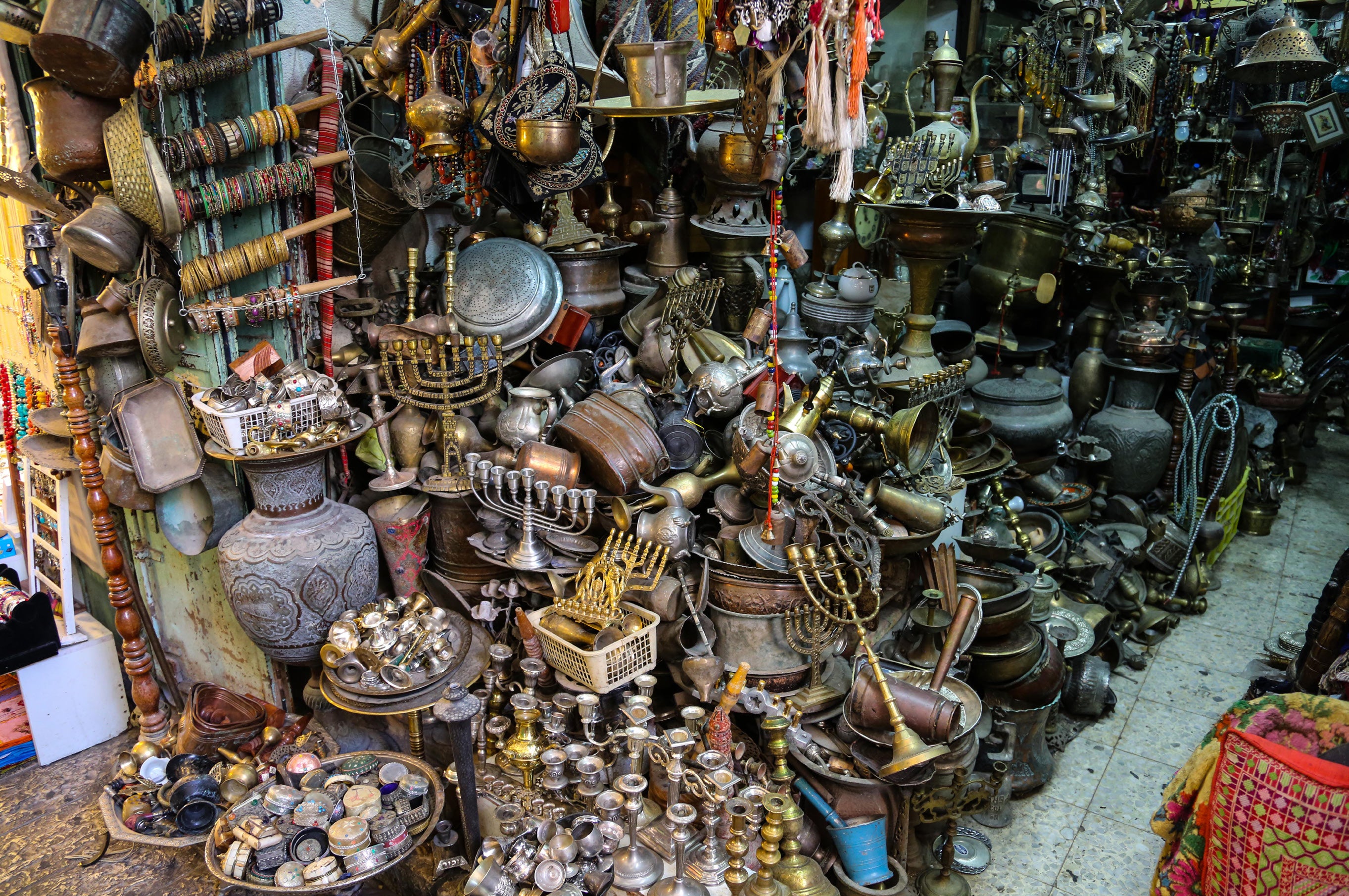 Dense display of antique brass menorahs lanterns vases and metalwork crammed into a flea market stall in Jaffa