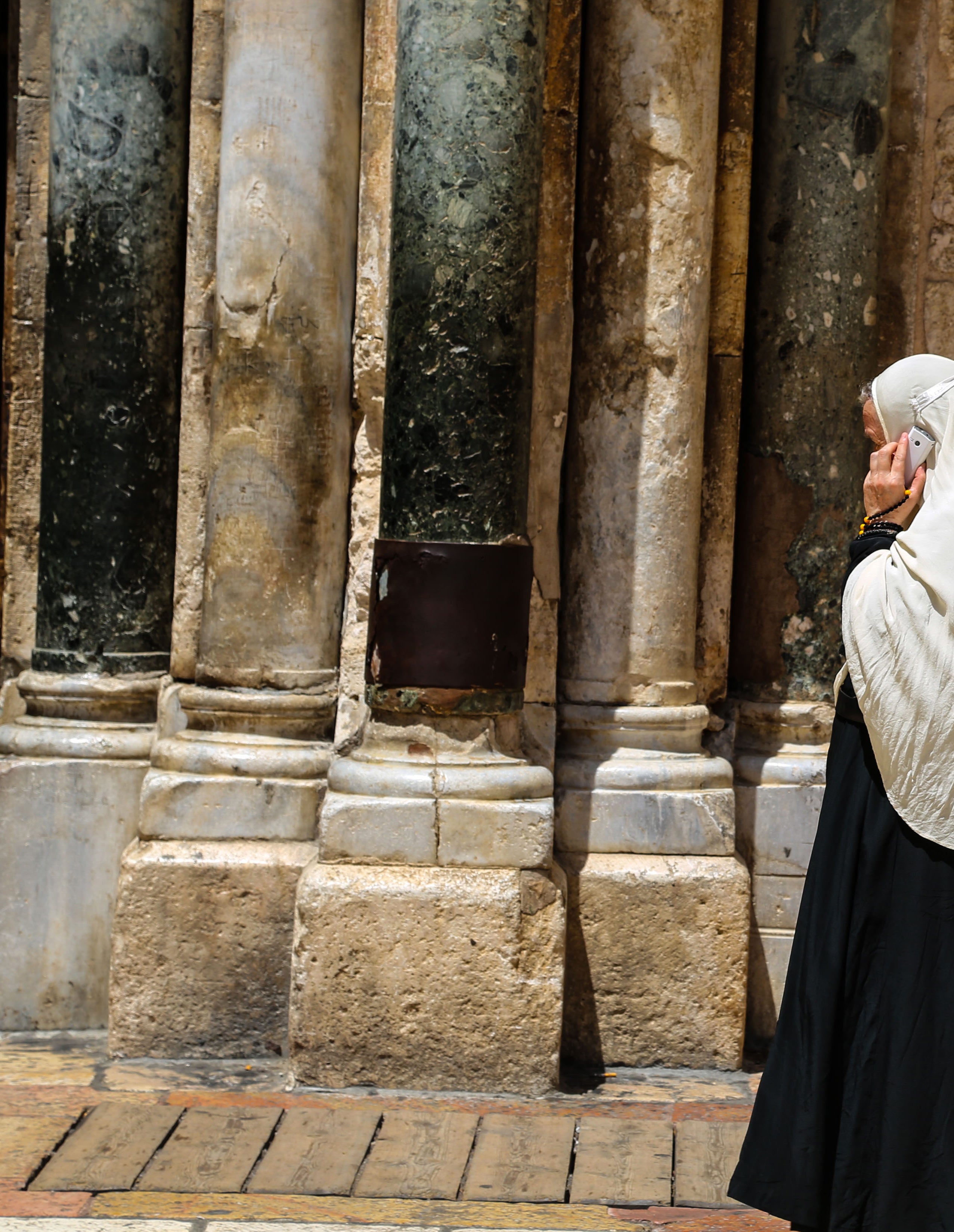 Woman in a headscarf walking past the weathered stone columns at the entrance of the Church of the Holy Sepulchre in Jerusalem