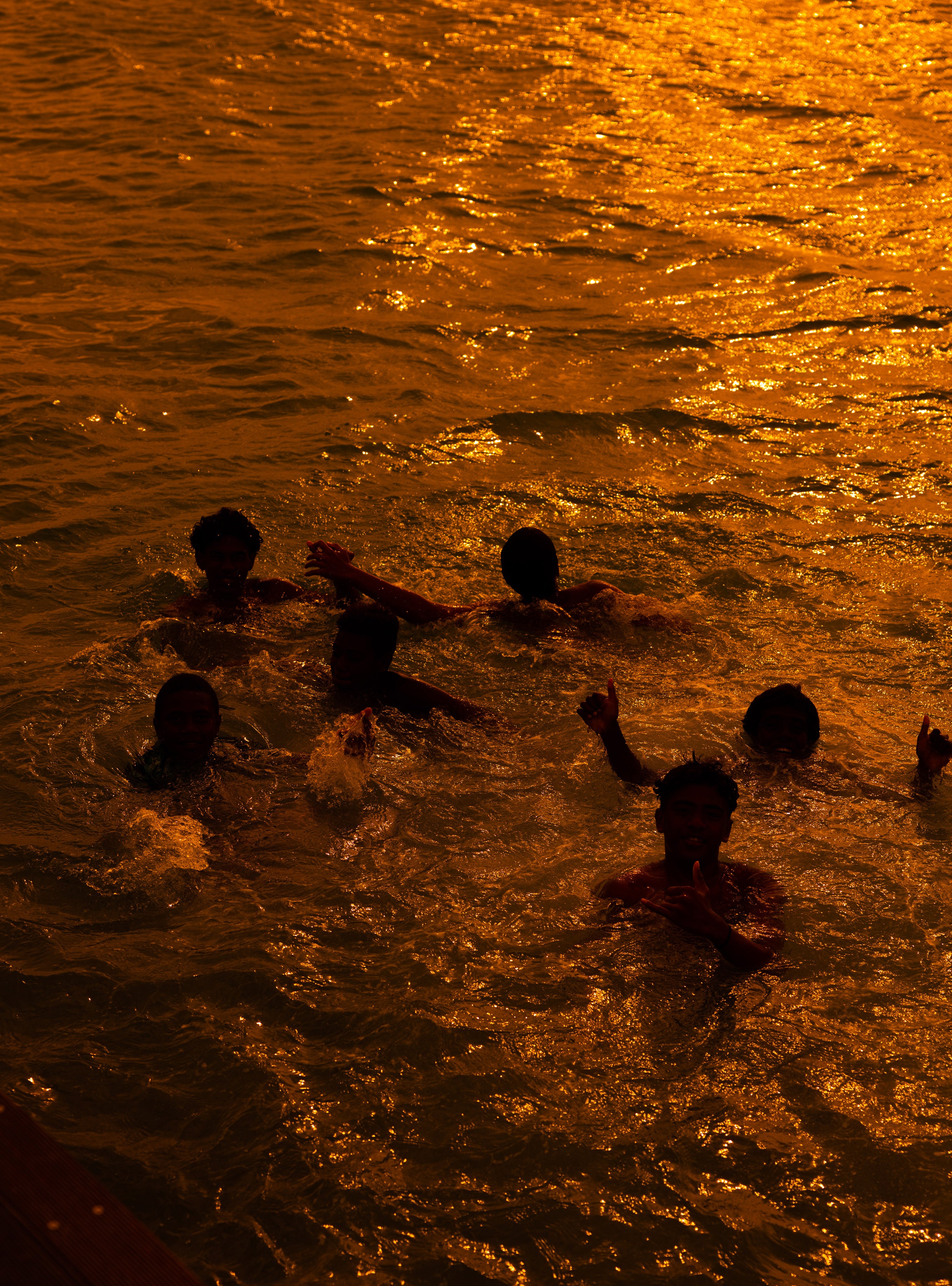 Silhouettes of children swimming and playing in shallow ocean water reflecting intense golden sunset light